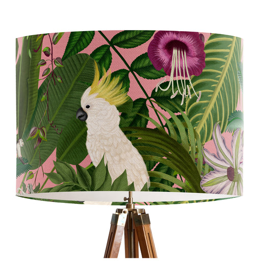Parrots in white, green & blue along with monkeys sit amoungst green tropical leaves on a pink background on a classic sized 30x21cm handcrafted fabric lampshade by artist Kelly Stevens-McLaughlan
